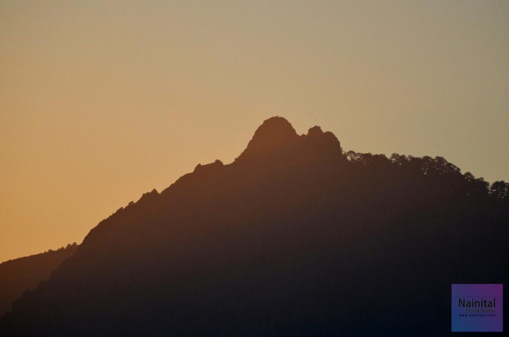 The Hidden "NAINITAL" **Alt Text:**
*Silhouette of Camel's Back ridge in Hidden Nainital during sunset, with rugged mountain peaks outlined against a warm golden-orange sky, creating a serene Himalayan landscape.*
